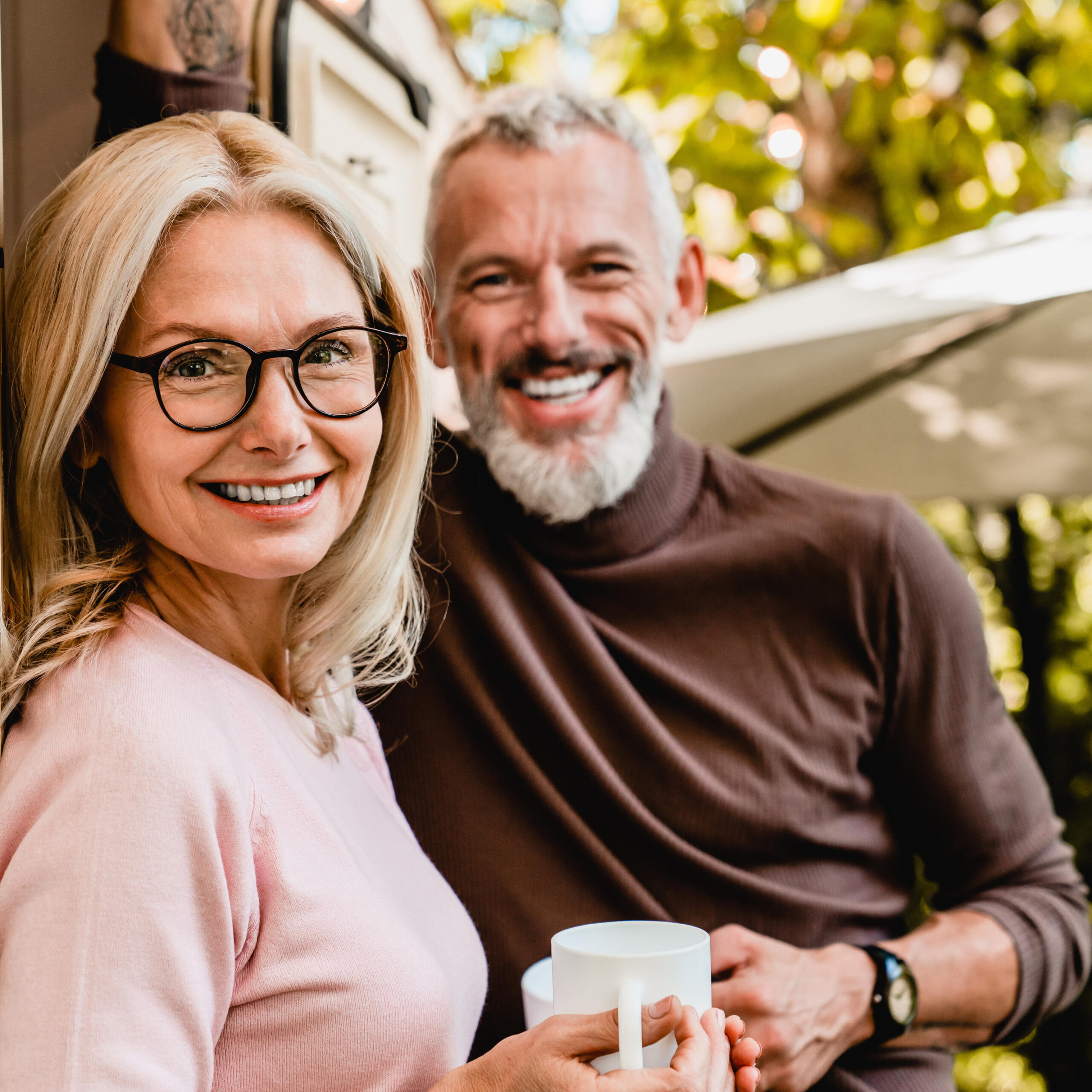 Close up shot of pleased senior caucasian couple smiling at the camera with cups of coffee standing in the van doorway